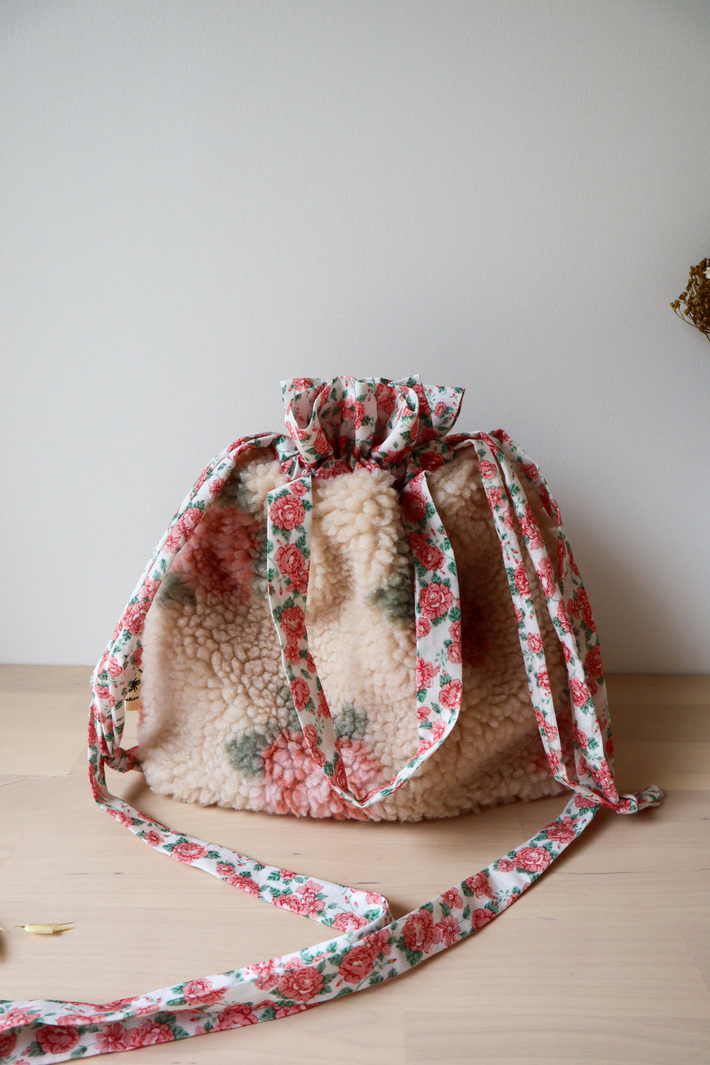 Vue rapprochée du sac bourse en fausse fourrure beige à fleurs roses, avec anses et bandoulière fleuries