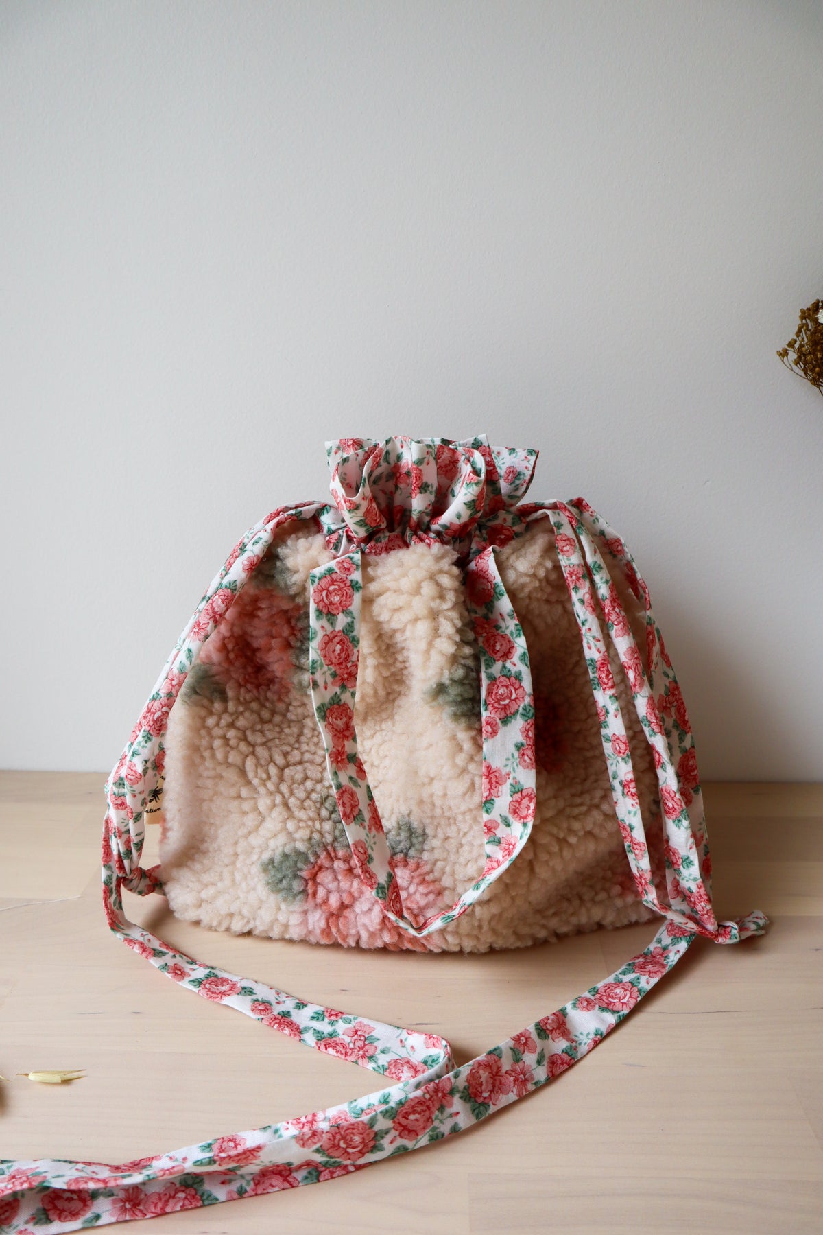 Vue rapprochée du sac bourse en fausse fourrure beige à fleurs roses, avec anses et bandoulière fleuries