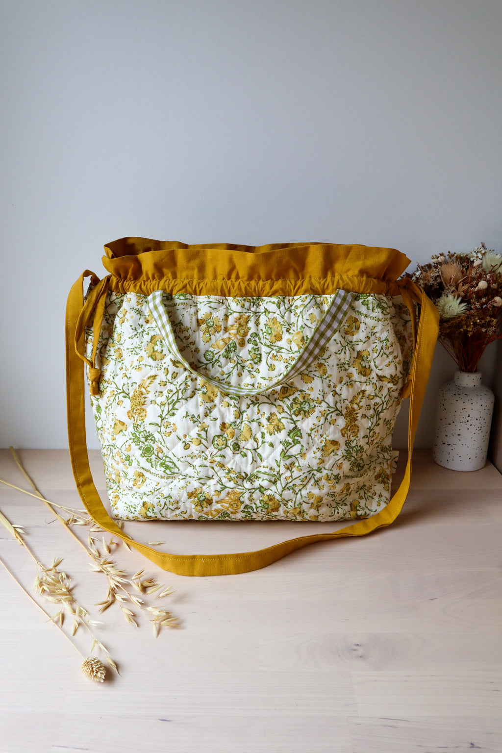 Grand sac bourse ouvert en tissu fleuri jaune et vert, avec bandoulière moutarde et petites anses à carreaux