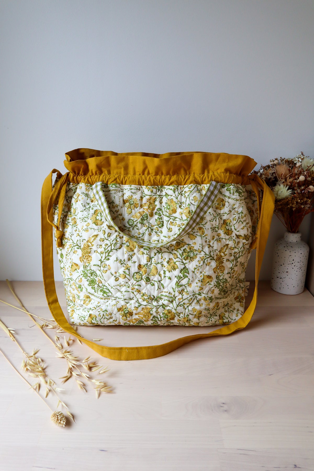 Grand sac bourse ouvert en tissu fleuri jaune et vert, avec bandoulière moutarde et petites anses à carreaux