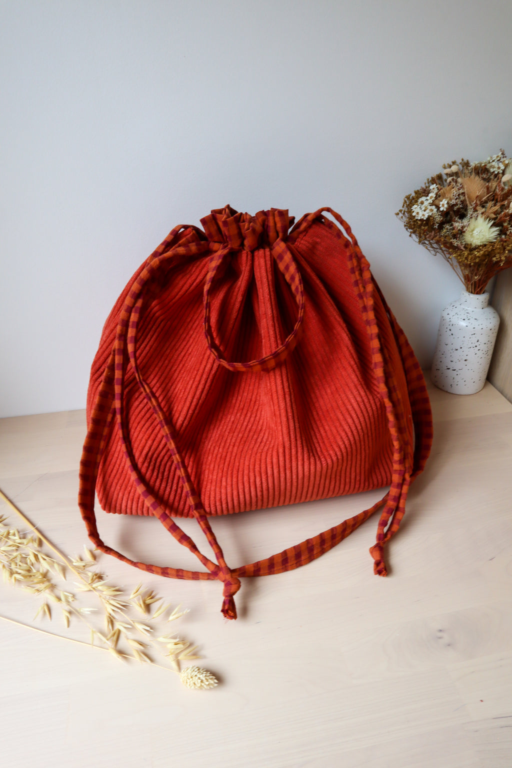 Sac bourse en velours côtelé rouge brique, avec petites anses, bandoulière et cordons en tissu à carreaux